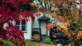 White cottage with blue trim, fall colored trees around