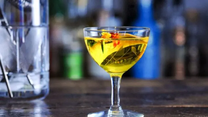 Yellow cocktail in coupe with edible flowers