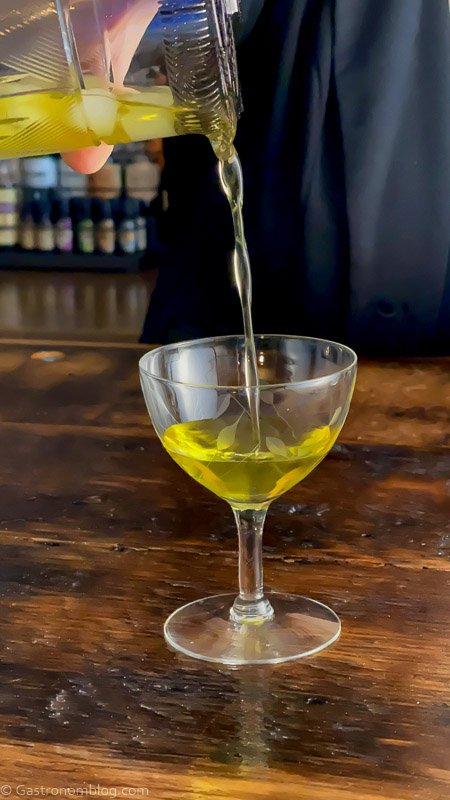White Negroni being poured into coupe from mixing glass