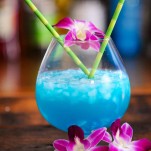 Blue Curacao cocktail in bulb glass with bamboo straws and purple and white orchids
