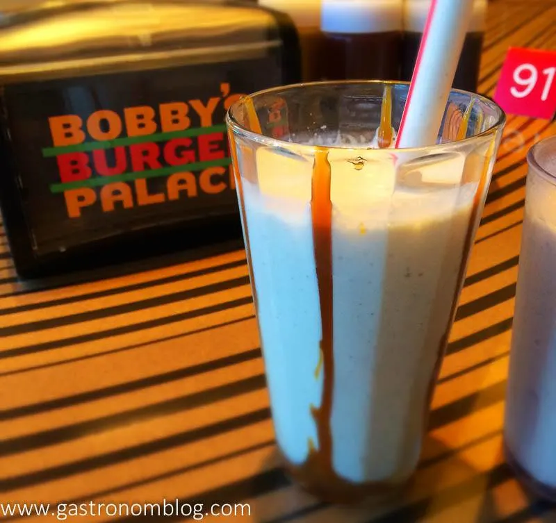 Milkshake with caramel on side of glass, with a straw at Bobby's Burger Palace