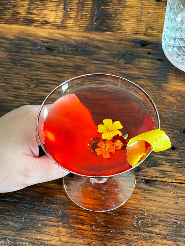top shot of red Old Pal cocktail recipe in coupe with edible flowers and lemon peel