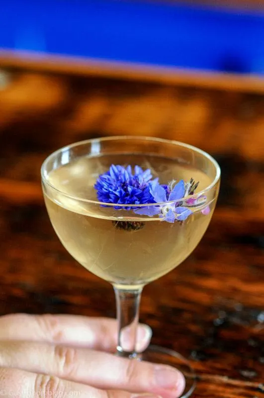 opaque cocktail in coupe with purple flower on top