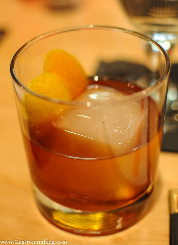 Brown cocktail over ice cube with orange peel in a rocks glass