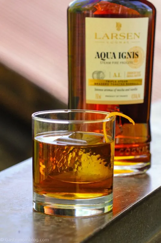 Cognac Old Fashioned in rocks glass with orange peel, cognac bottle behind