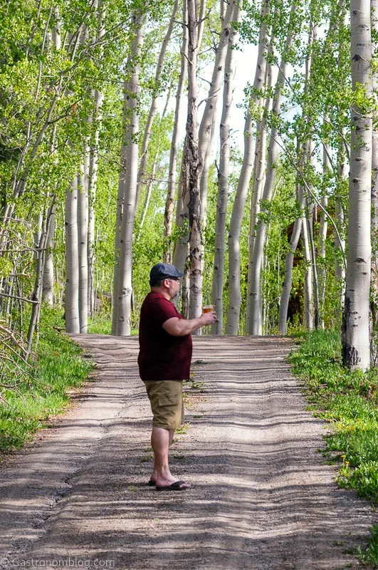 Man in maroon shirt holding Cognac Old Fashioned with orange peel on the rim in an aspen grove