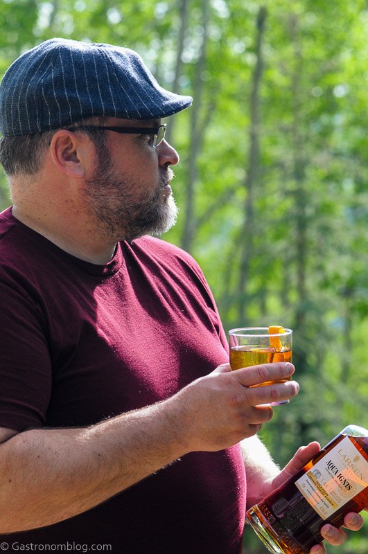 Man in maroon shirt holding Cognac Old Fashioned with orange peel on the rim