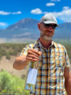 Steve Steese holding white wine bottle in front of mountains at Storm Cellar Winery