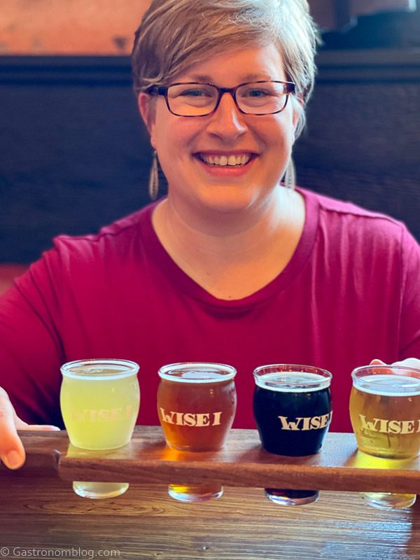 Woman in glasses and maroon top with beers to taste at Wise I Brewery for the Iowa Brewery Tour and Iowa Beer Passport