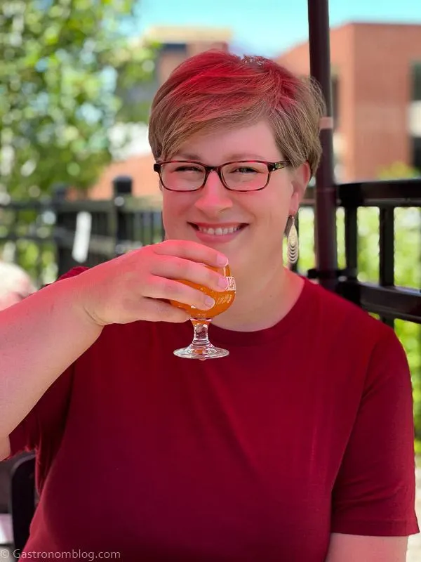 Woman in maroon top and glasses holding beer