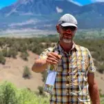 Steve Steese holding white wine bottle in front of mountains at Storm Cellar Winery