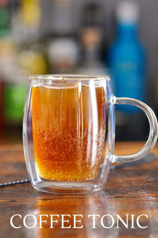 Brown coffee tonic in glass mug with handle and clear ice cube
