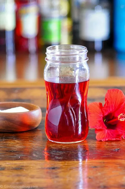 Red Hibiscus syrup in a glass jar with red Hibiscus flower and wooden bowl of sugar