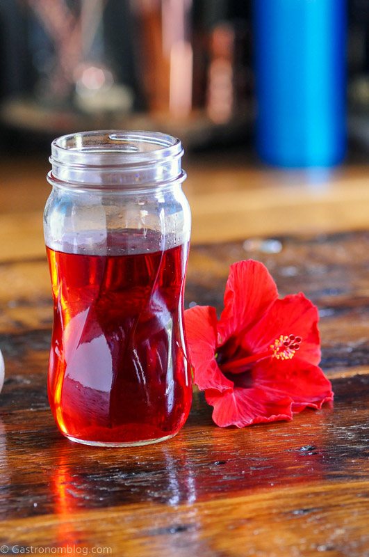 Red Hibiscus syrup in a glass jar with red Hibiscus flower and wooden bowl of sugar