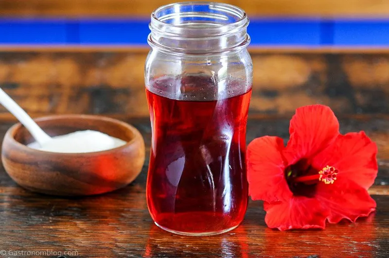 red syrup in a jar with a red flower and wooden bowl of sugar