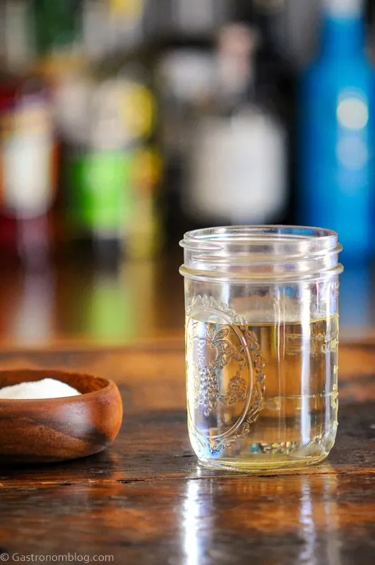 Simple syrup, clear syrup in mason jar, wood bowl with sugar and white spoon