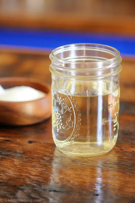 Clear syrup in mason jar, wood bowl with sugar and white spoon