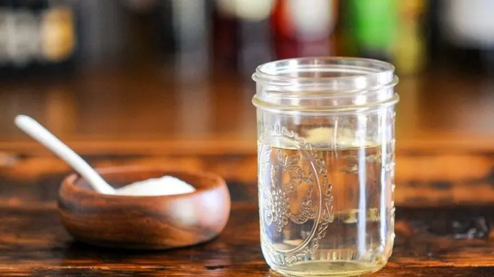 Clear syrup in mason jar, wood bowl with sugar and white spoon