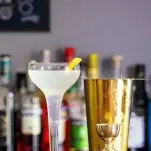 French 75 cocktail in coupe with lemon peel and gold bar tools
