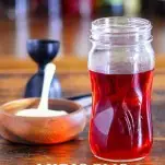 Red Hibiscus syrup in a glass jar with red Hibiscus flower and wooden bowl of sugar