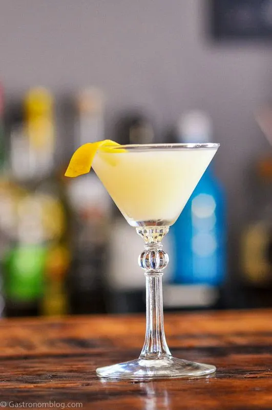 Peach Aquavit Yellow cocktail in coupe, orange peel on wood table