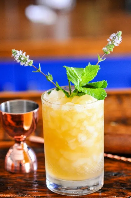 Orange cocktail in double rocks glass, mint leaves, brass barware behind