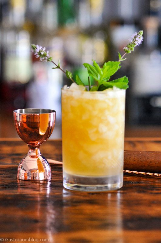 Orange cocktail in double rocks glass, mint leaves, brass barware behind