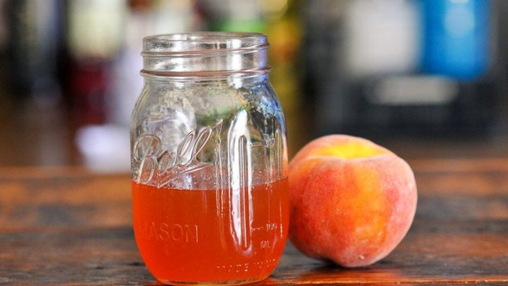Peach colored syrup in jar on wood table, peach next to jar