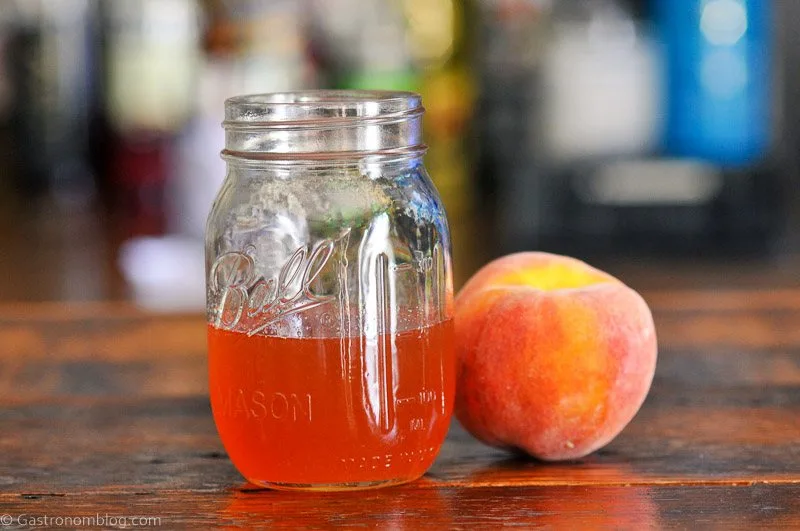 Peach colored syrup in jar on wood table, peach next to jar