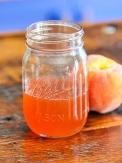 Peach colored syrup in jar on wood table, peach next to jar