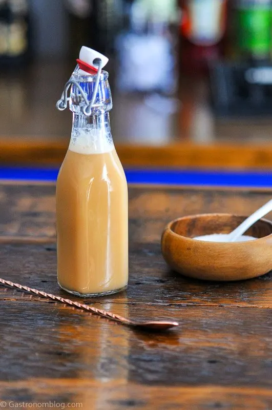 Tan liqueur in a swingtop bottle, a Salted Caramel Vodka has a wooden bowl of salt next to it with a white spoon