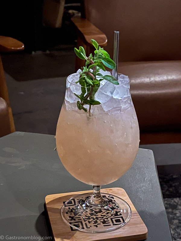 Pink cocktail with pebble ice and sprig of mint on wooden coaster