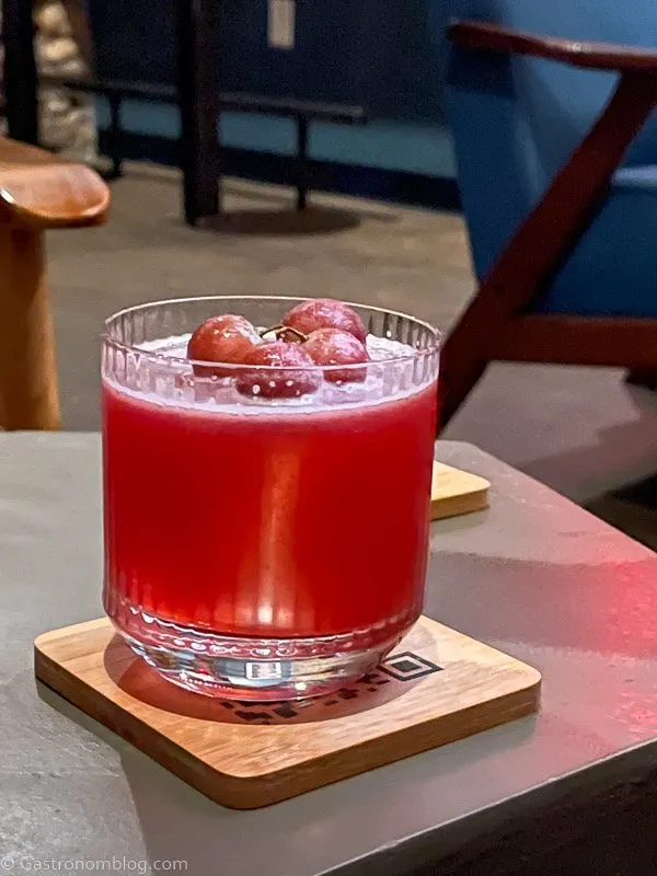 Pink cocktail in rocks glass with grapes on top on wooden coaster