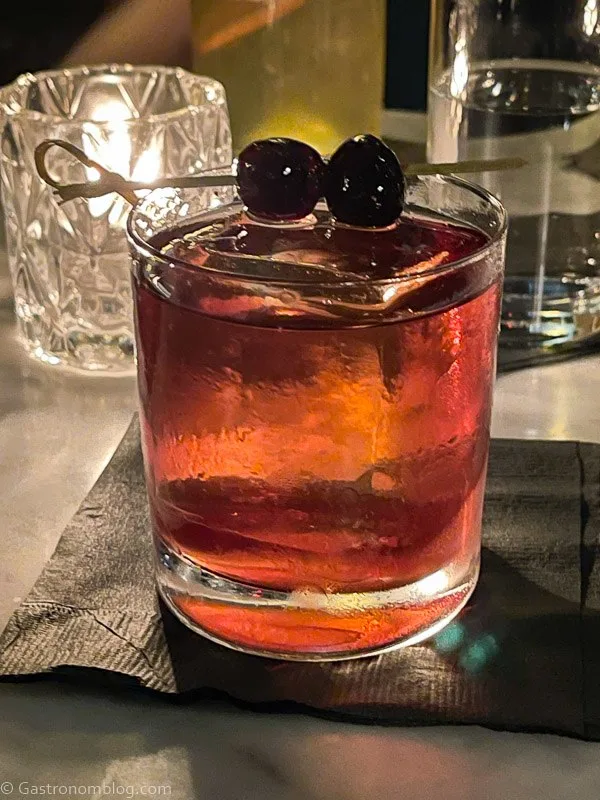 Brown cocktail in glass with ice and cherries on pick