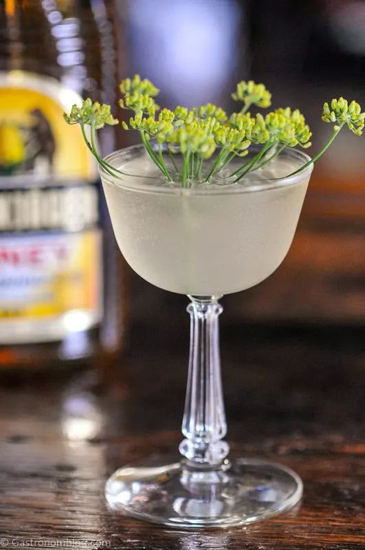 Yellow cocktail in coupe with dill flower, Barenjager honey liqueur bottle behind