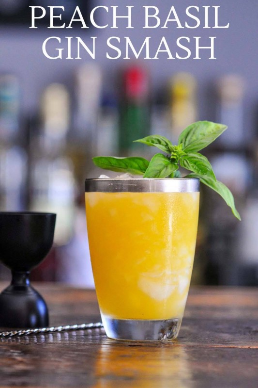 orange cocktail in silver rimmed glass, basil garnish, black jigger and bar spoon