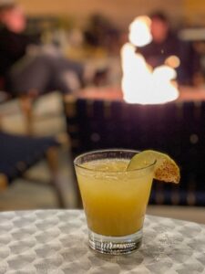 Yellow cocktail on table, fire in background