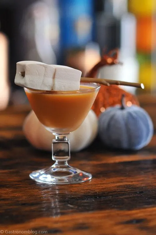 Pumpkin Salted Caramel Martini in coupe, marshmallows on stick garnish, orange liqueur bottle behind