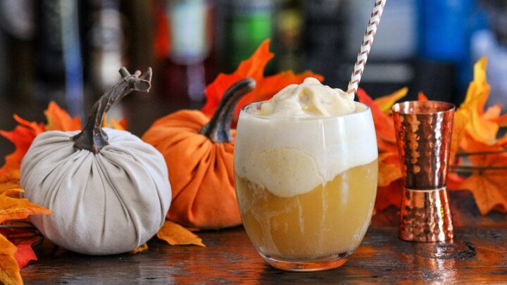 Orange Pumpkin Ice Cream Float in glass, topped with white foam, striped straw, pumpkins and brass jigger