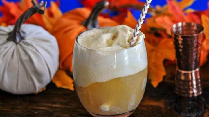 Pumpkin Ice Cream Float in glass, topped with white foam, striped straw, pumpkins and brass jigger