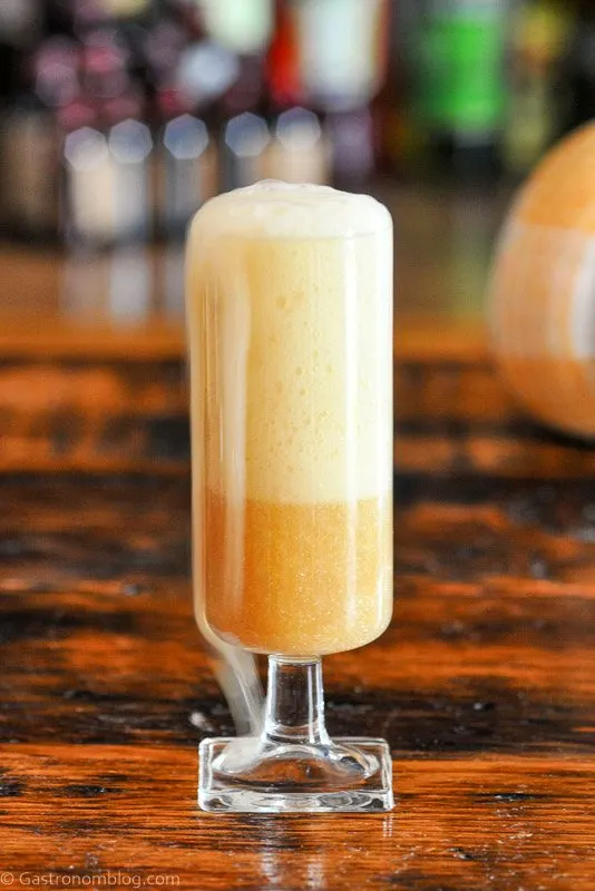 tan colored cocktail in glass with foam from champagne