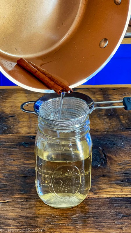 cinnamon simple syrup being poured into jar from a copper saucepan