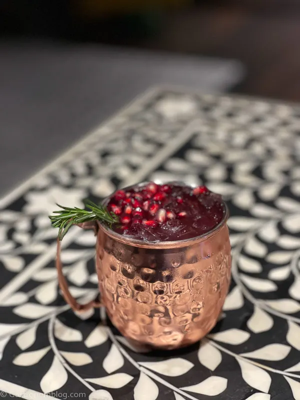 copper mug cocktail with pomegranate arils on black and white print table