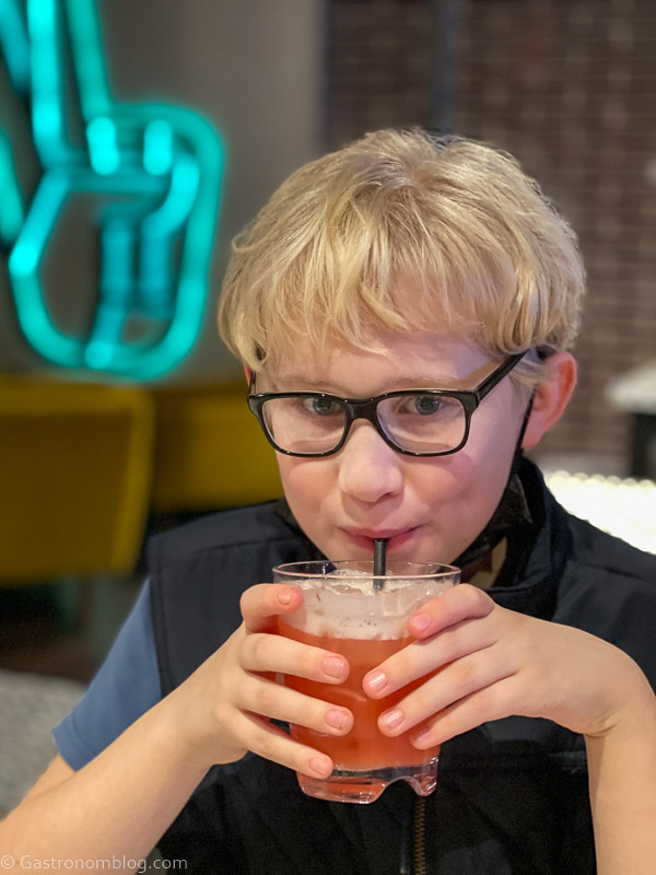 blonde boy with glasses drinking a pink mocktail