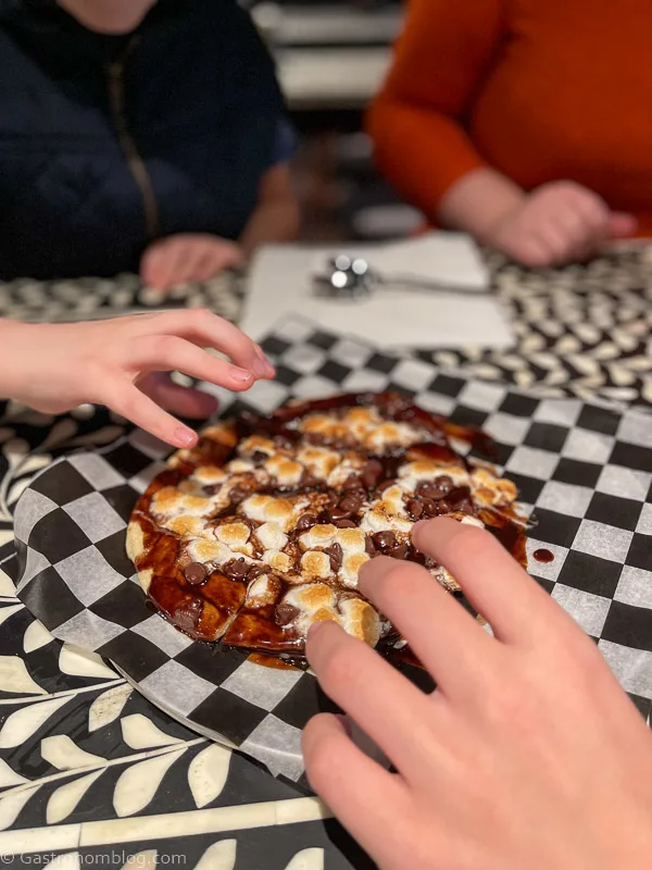 hands reaching for a s'mores pizza with chocolate and marshmallows