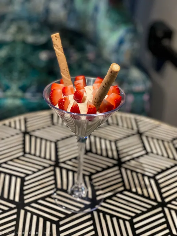 Tall glass with white pudding, strawberries and tall cookies on black and white pattern table