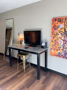 Table with tv, gold stool, mirror and orange picture on wall