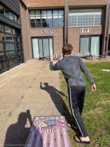 boy throwing beanbag playing cornhole outside