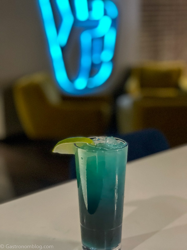 Blue green cocktail on white bar with neon sign behind