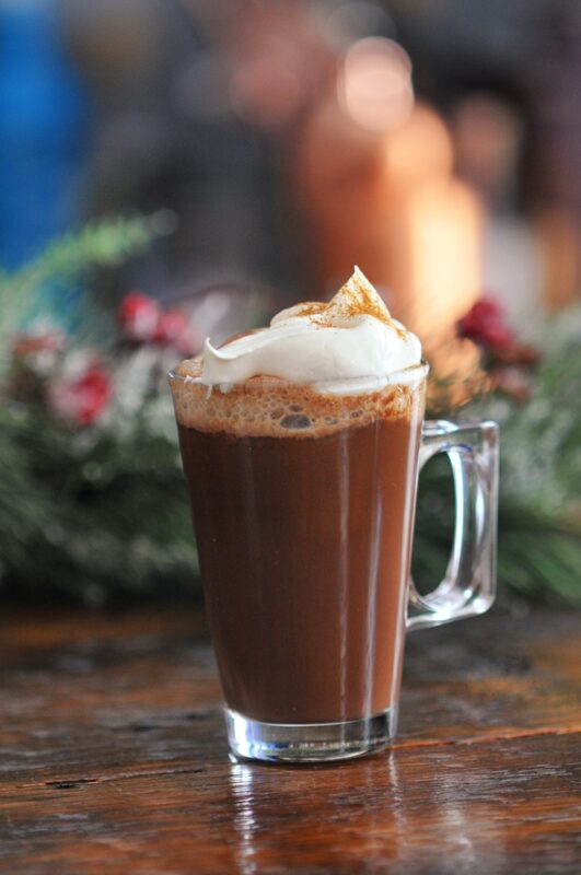 Chartreuse Hot Chocolate in glass mug with whipped cream, foliage behind